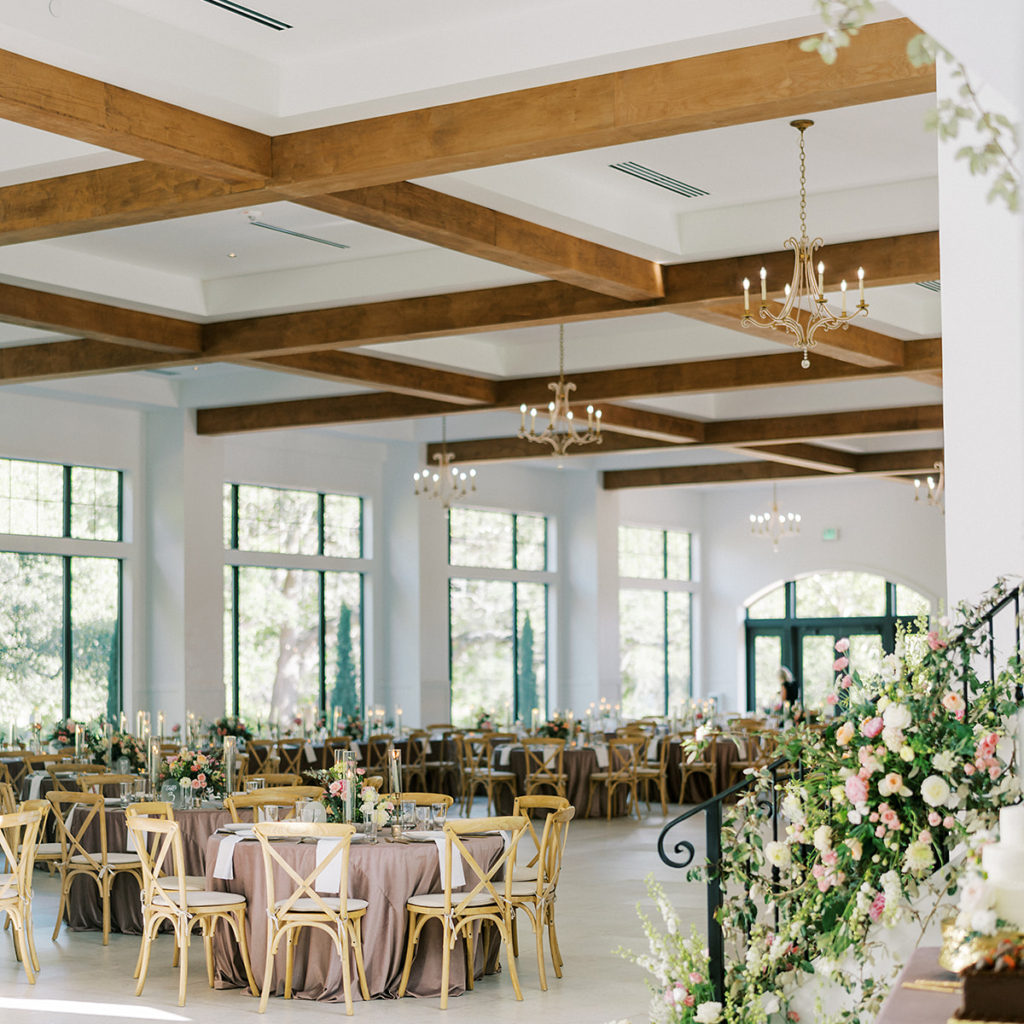 Reception Ballroom with large windows on the back wall, staircase railing, and tables decorated with linens candles and floral arrangements