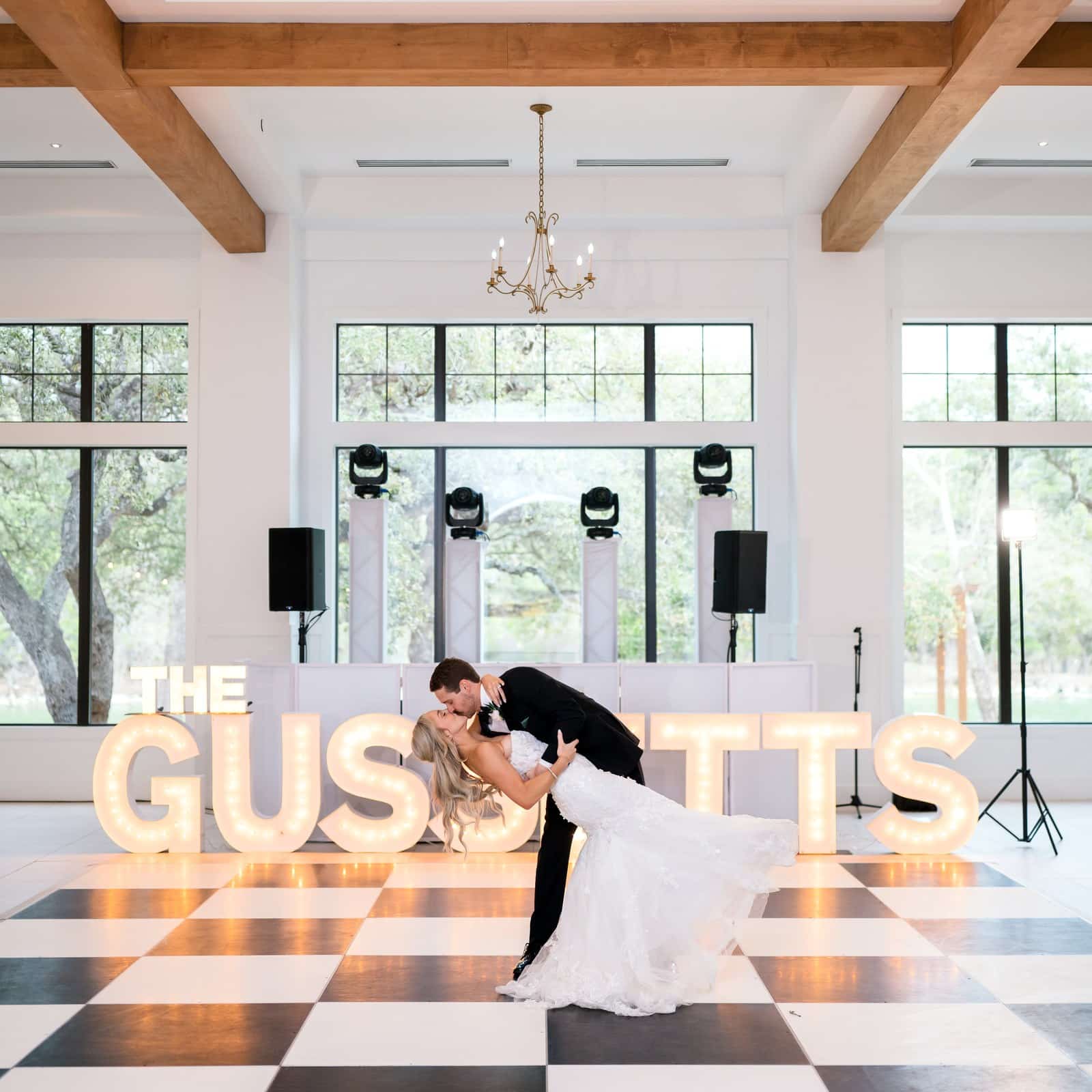 Bride and groom dip kiss on a black and white checkered dance floor in front of lighted marquee letters in the ballroom