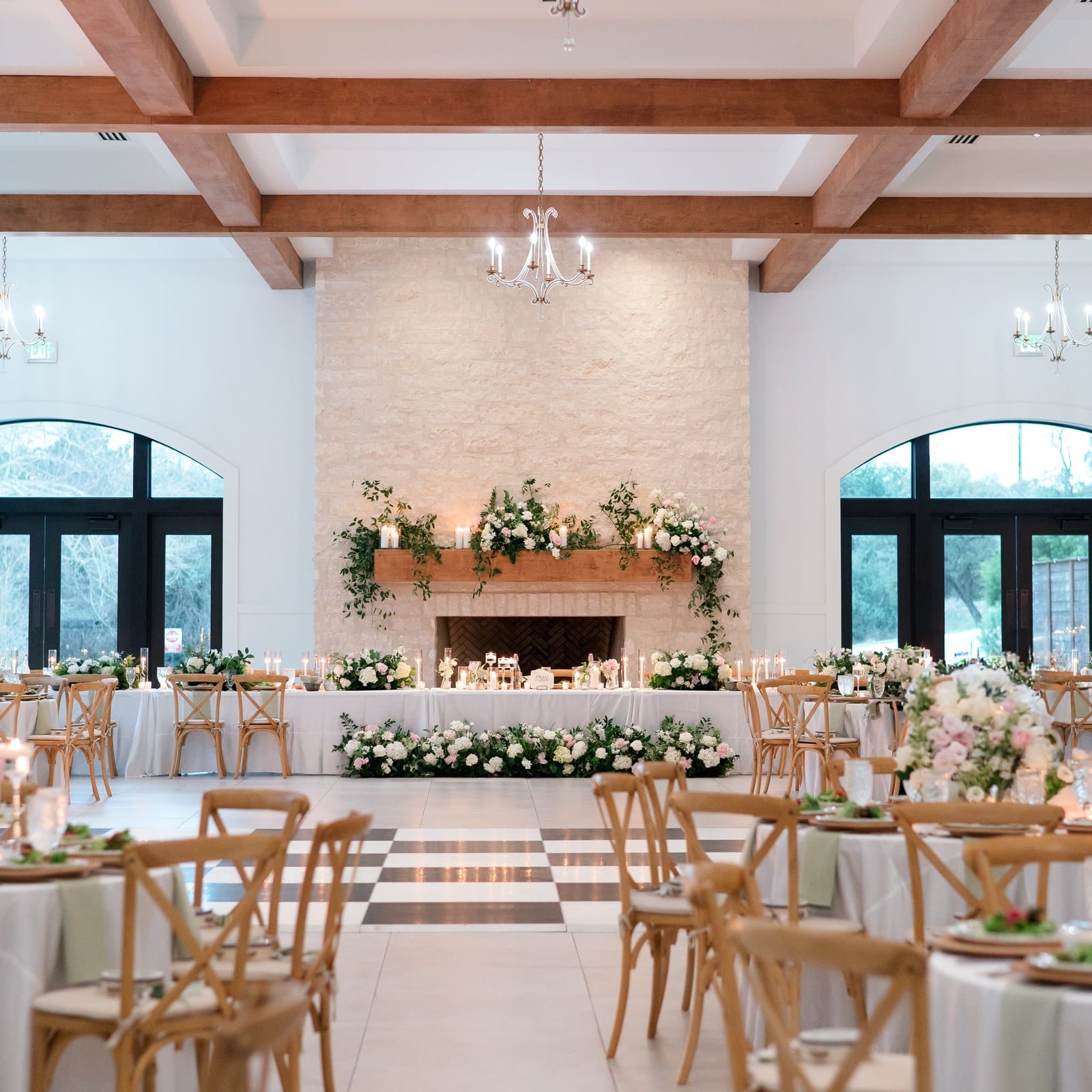 Head table in front of the stone fireplace in The Preserve at Canyon Lake ballroom, with white and blush florals and a checkered dance floor