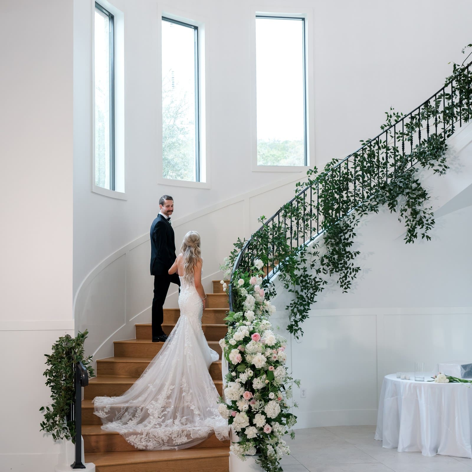 Bride and groom on the spiral staircase in The Preserve at Canyon Lake ballroom, with greenery and white florals along the railing