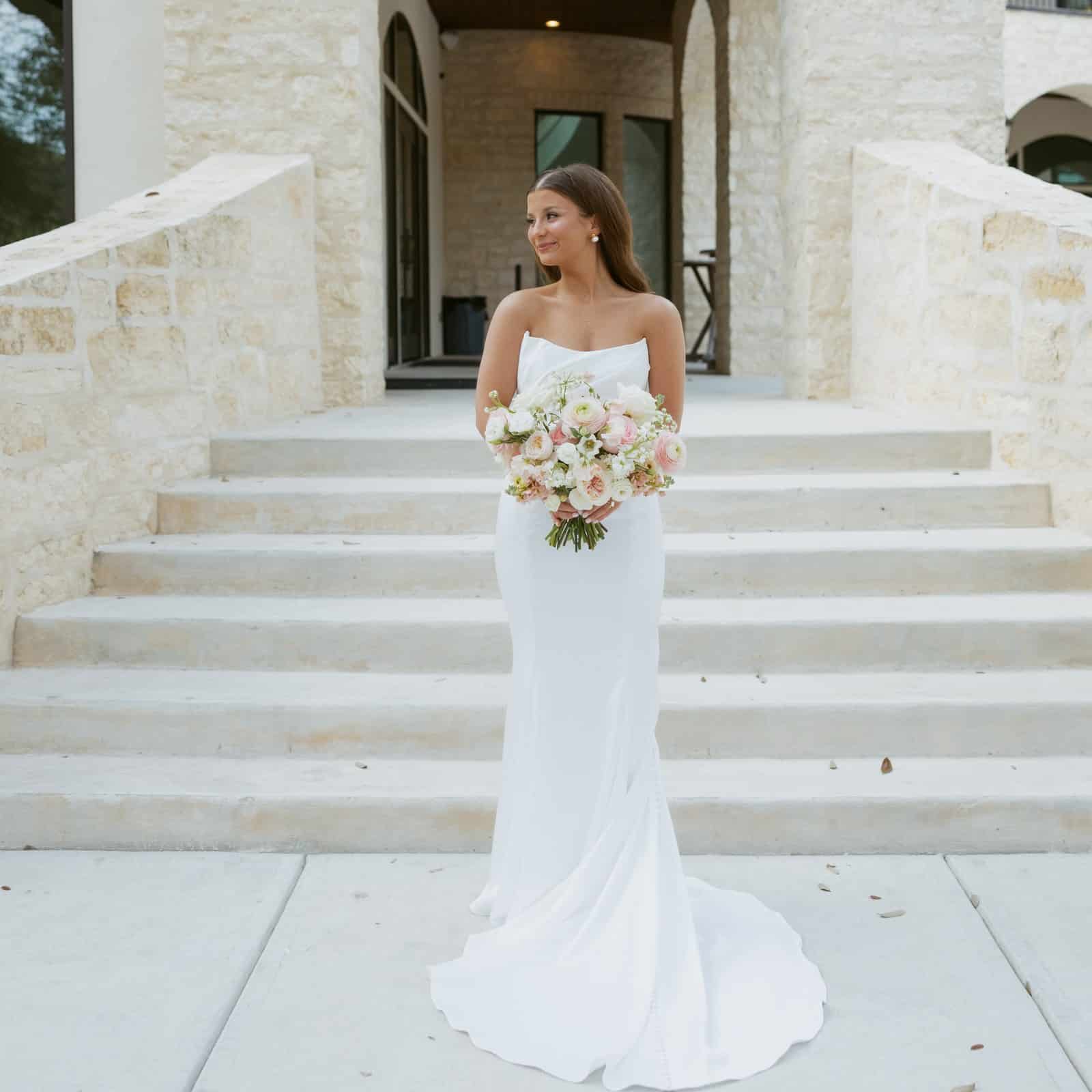 Bride holding a blush and white bouquet on the front steps of The Preserve at Canyon Lake